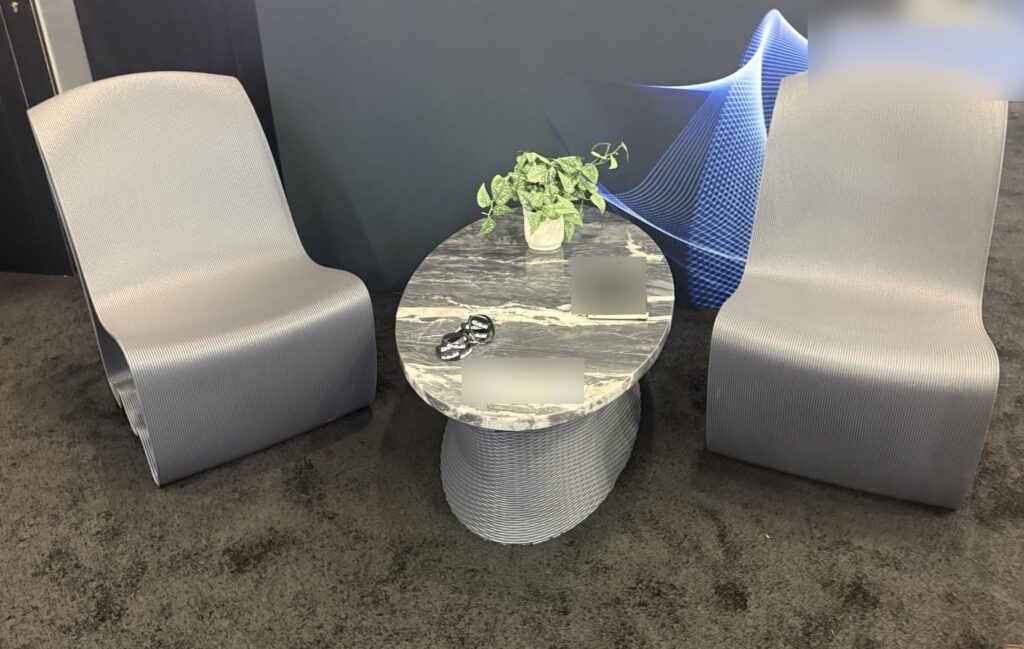 Large-format 3D printed lounge chairs and table base at an industry trade show